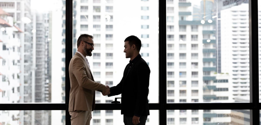 Silhouette business man handshaking with Asian male customer to greeting or dealing agreement in the modern office