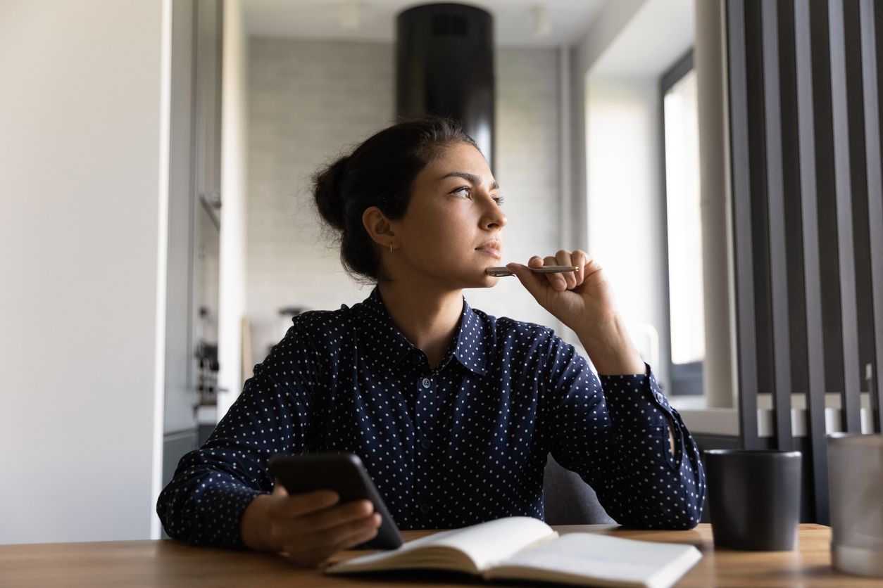 woman pondering looking out the window with notebook