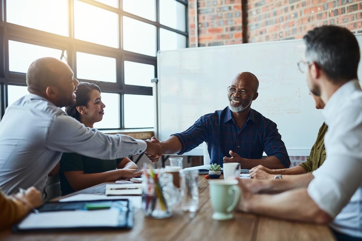 employees sitting at table, two shaking hands