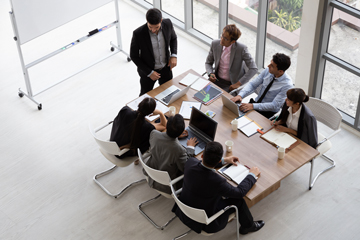 businesspeople in strategy session seated at conference table with leader standing in front of whiteboard