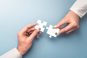 two peoples hands holding connecting puzzle pieces near each other