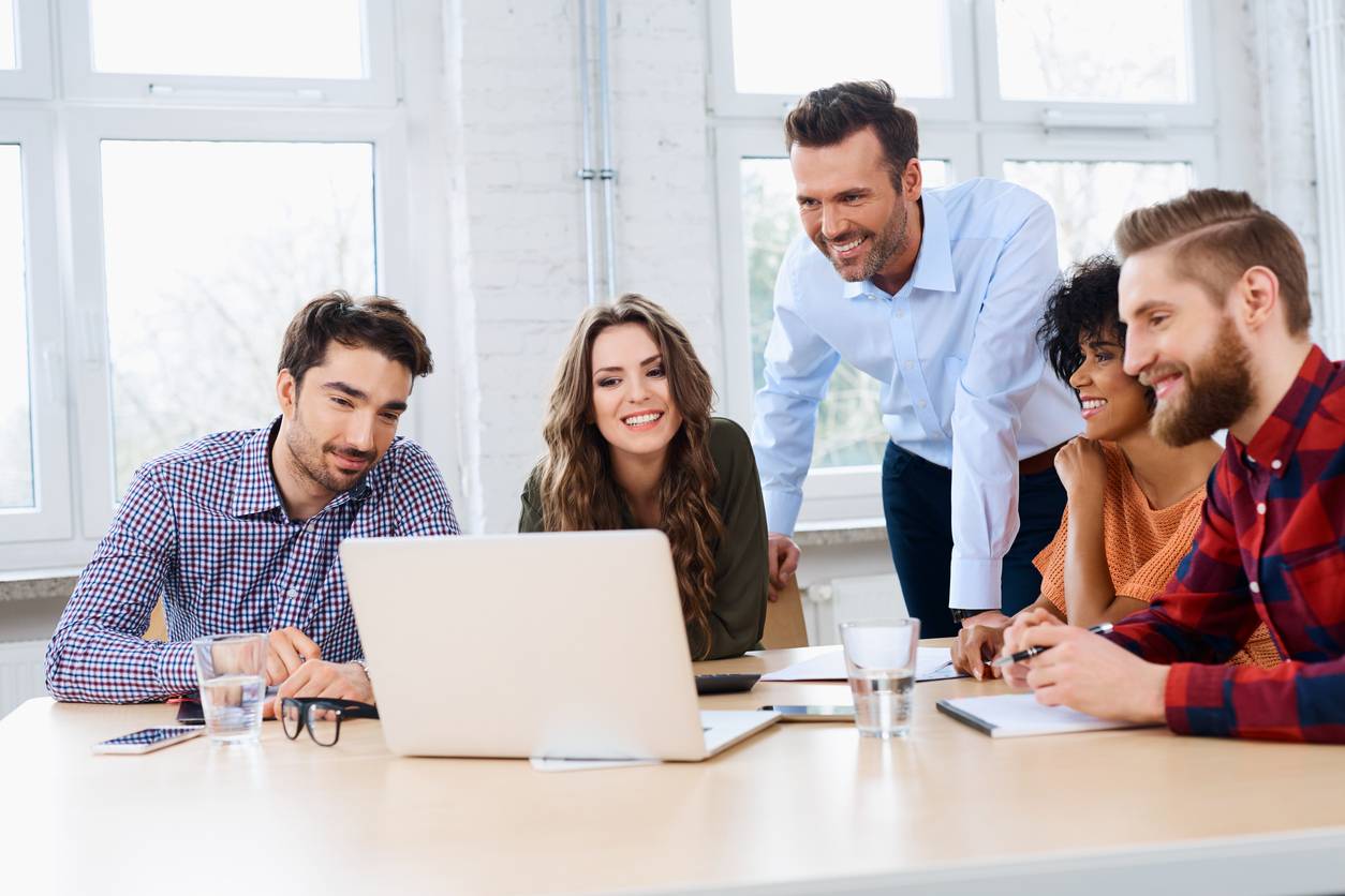 team sitting at a table gathered around a laptop